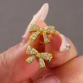 Funkelnde vergoldete Schleifenohrringe mit Zirkonia-Mikropavé in der Hand gehalten - Gold