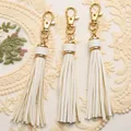 Detailed view of three white PU leather tassels with gold lobster clasps and lace background - White