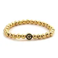Detail of golden beaded elastic bracelet featuring a black bead with a gold letter G - G-Shape Style