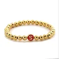 Detail of golden metal beaded elastic bracelet with a red round initial S charm pendant - Letter S Style