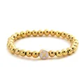 Detail of golden beaded elastic bracelet featuring a white round charm with letter X - Letter X Style