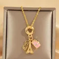Goldene Halskette mit Eiffelturm, rosa Kamera und Brillenanhänger auf Satin-Hintergrund - Kamera Brille Eiffelturm Kombination Stil (XL3356)