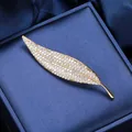 Spilla a foglia dorata con pavé di zirconi bianchi su elegante sfondo di seta blu - Oro