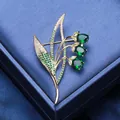 Elegant gold flower brooch with green gemstones and zircon micro-pave on a blue box - Green