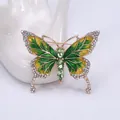 Détail d'une broche papillon en émail vert avec dorure et strass brillants sur fond blanc - Vert