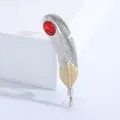 Détail d'une broche plume bicolore argent et or avec une pierre rouge sur fond blanc - Rouge
