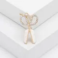 Elegante broche de tijera con diamantes de imitación y nácar sobre soporte blanco - Dorado