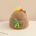Close-up of baby knit hat with colorful dinosaur fins and a cute letter patch detail - 2-6 Years Old / Light Coffee