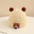 Dettaglio del berretto in maglia beige per neonati con orecchie e piccolo stemma a orsetto - Neonato circa 2-6 anni / Beige