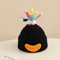 Close-up of black knitted winter hat with colorful pom-poms and funny cartoon eyes - 2-6 Years Old / Black