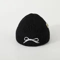 Close-up of black ribbed knit beanie featuring white bow embroidery and side fabric label - Baby Approx 2-6 Years / Black