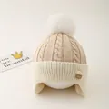 Close-up of cable knit earflap hat for kids featuring a large white faux fur pompom - One Size / Deep Beige