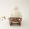 Detail of knit child hat with pompom ear flaps and Choco biscuit patch decoration - One Size / Light Beige