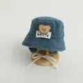 Close-up of blue lamb wool bucket hat with brown bear patch and white chin straps - 48-52cm / Blue