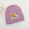 Dettaglio del berretto in maglia viola per neonati con toppa a orsetto e etichetta Lucky - Bambini 2-6 Anni Elastico / Viola