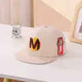 Detailaufnahme der beigen Snapback-Kappe für Kinder mit M-Stickerei auf dem Tisch - Kinder ca. 3-10 Jahre / Beige