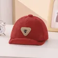 Detail of baby corduroy baseball cap in brick red showing soft brim and letter patch - 45-48cm / Burgundy