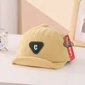 Close-up of beige corduroy baby cap with green 'C' letter patch on a warm decor background - 45-48cm / Yellow