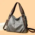 Close-up of grey leather handbag with brown handles and white cross-stitching detail - Gray