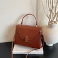Brown lychee texture tote bag with golden buckle and crossbody strap on a book - Brown