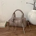 Khaki Boston shoulder bag with rivet studs and woven tassel details on wooden table - Tan