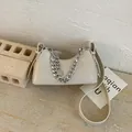 Chic cream croissant crescent bag with silver chain strap on a textured stone display - White