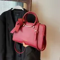 Red leather bucket bag with round handle and large bow detail against black blazer - Red