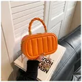 Detail of orange quilted box bag with twisted handle and gold chain on books - Orange