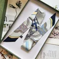 Details eines bedruckten Seidenschals mit Reitmotiven in einer grünen Geschenkbox - Nude