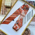 Close-up of a folded silk twilly scarf with paisley and star patterns in a gold gift box - 5x90cm / Orange and Beige
