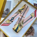 Detail eines rosa Seidenschals mit Kettenmuster, gefaltet in einer gelben Luxus-Geschenkbox - Langes Band / Rosa