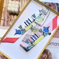 Detail of printed silk twilly scarf with blue bird pattern next to yellow gift box - 90x5cm / Red (S919)