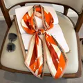 Long silk scarf with horse print and chevron pattern draped over a book on a chair - Striped Pony Large Asymmetrical Scarf - Orange Red