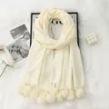 Close-up of cream faux cashmere scarf featuring soft pom-pom tassels and cozy knit texture - Creamy White