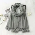 Detail of grey cashmere-feel scarf with fluffy pompom decor and fringe on white fur rug - Light Gray