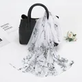 Détail d'une écharpe en mousseline imprimée fleurie drapée sur un sac à main en cuir noir - Modèle Châle Long (XQ377) / 150*50cm / Gris-Blanc à Fleurs Grises