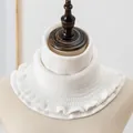 Detail of white knitted neck warmer with waffle texture and elegant scalloped edge - White
