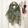 Detail view of branch print voile scarf draped on white blazer for a stylish look - Green