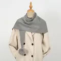 Detail eines grauen Strickschals mit Pompons gestylt auf einem beigen zweireihigen Mantel - 86*36cm / Grau