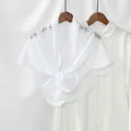 Detail of white floral lace shawl with scalloped edges draped on a wooden hanger - White