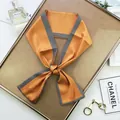 Détail d'un foulard étroit en soie orange avec motif à chevrons noué en un nœud élégant - Style Long / Orange