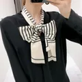 Elegante zwart-wit gestreepte smalle zijden sjaal gestrikt in een strik op een zwart shirt - Beige