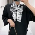 Detail van zwart-wit gestreepte zijden sjaal geknoopt in een grote strik op zwart t-shirt - Wit