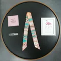 Detailed close-up of a long twilly silk scarf with vintage belt buckle pattern in pink and green - Khaki/Earth Yellow