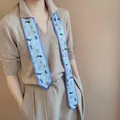 Detail van een blauwe zijden twilly sjaal met kleurrijke kattenprints gedragen door model - 7*130cm / Blauw