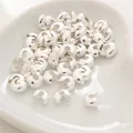 Vista macro di copri-schiaccini argentati su un vassoio bianco per creazione gioielli - 3mm (100 Pezzi/Confezione) / Argento