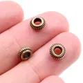Makroaufnahme von drei bronzenen 5mm Zwischenperlen auf einer Fingerspitze für DIY-Schmuck - 50 Stück (5mm) / Antikbronze