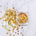 Macro shot of gold holographic butterfly nail sequins in a clear jar on white marble - Gold Holographic Butterfly Sequins Jar (HD-01)