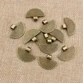 Detailed macro view of vintage bronze fan-shaped alloy pendants on natural beige burlap fabric - Bronze