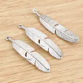Three silver alloy feather pendants for DIY jewelry making on a light wooden background - Antique Silver